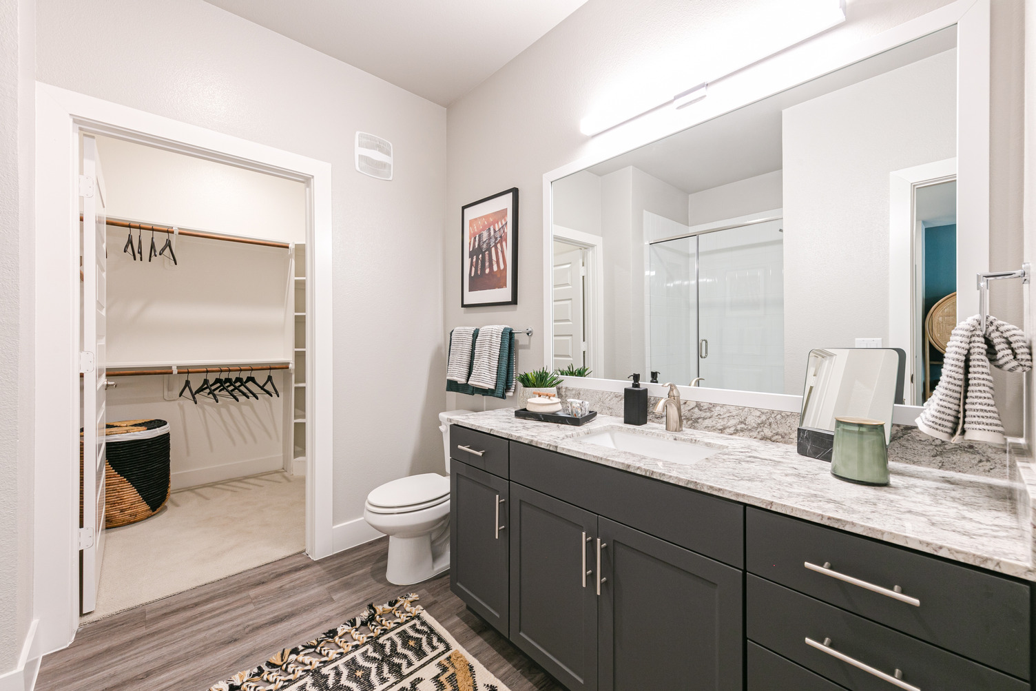 Model apartment bathroom with quartz countertop, framed glass mirror, and walk-in closet with shelving