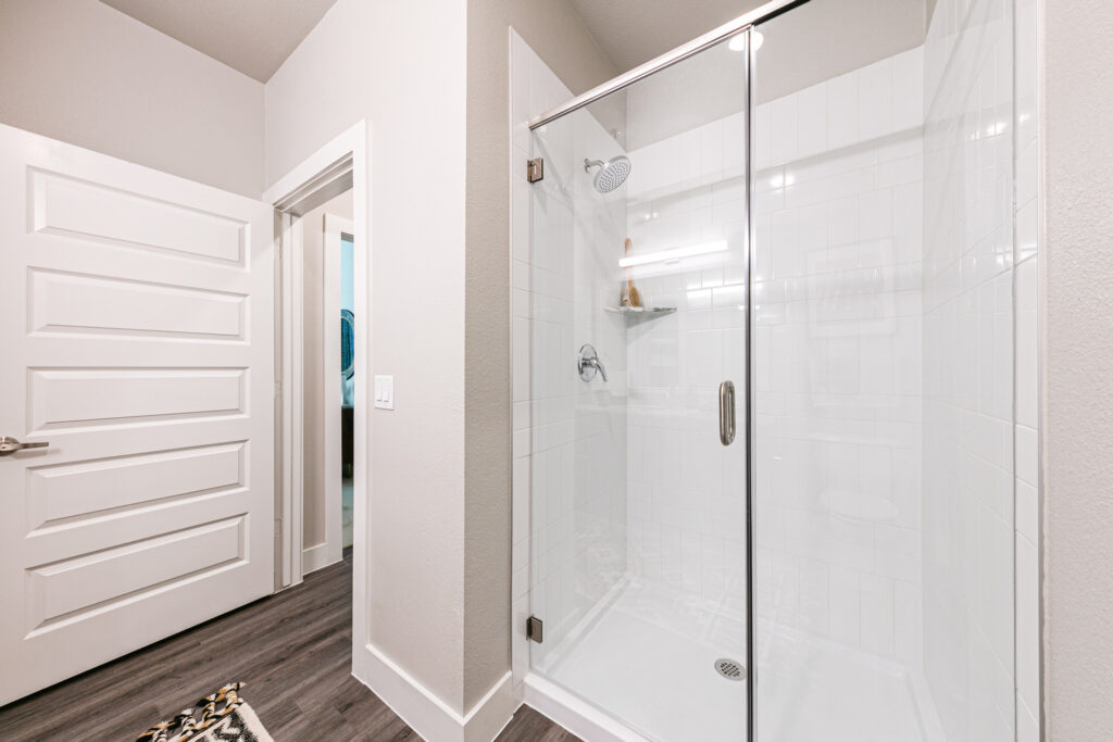 Walk-in shower with glass door and brushed nickel fixtures in model apartment bathroom