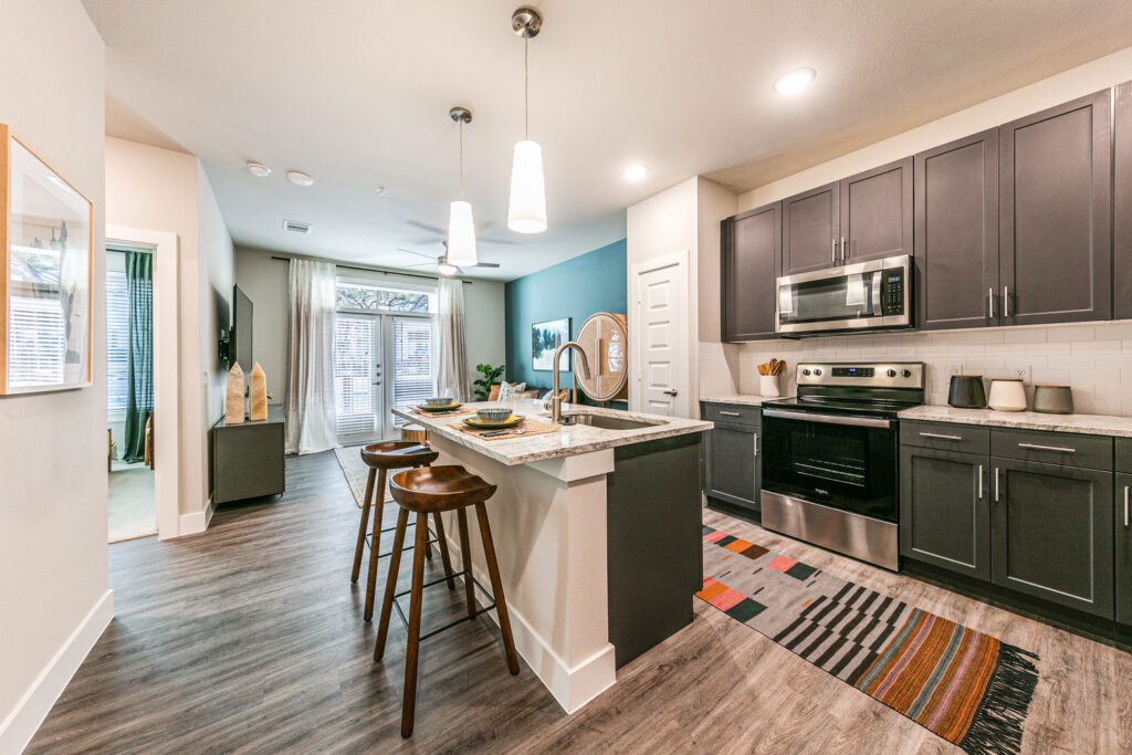 Model apartment with wood plank inspired flooring, dark cabinets, subway tile backsplash and kitchen island with barstool seating and pendant lighting