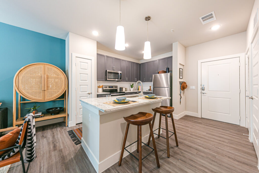 Model apartment kitchen with island, designer pendant lighting, stainless steel appliances, and pantry
