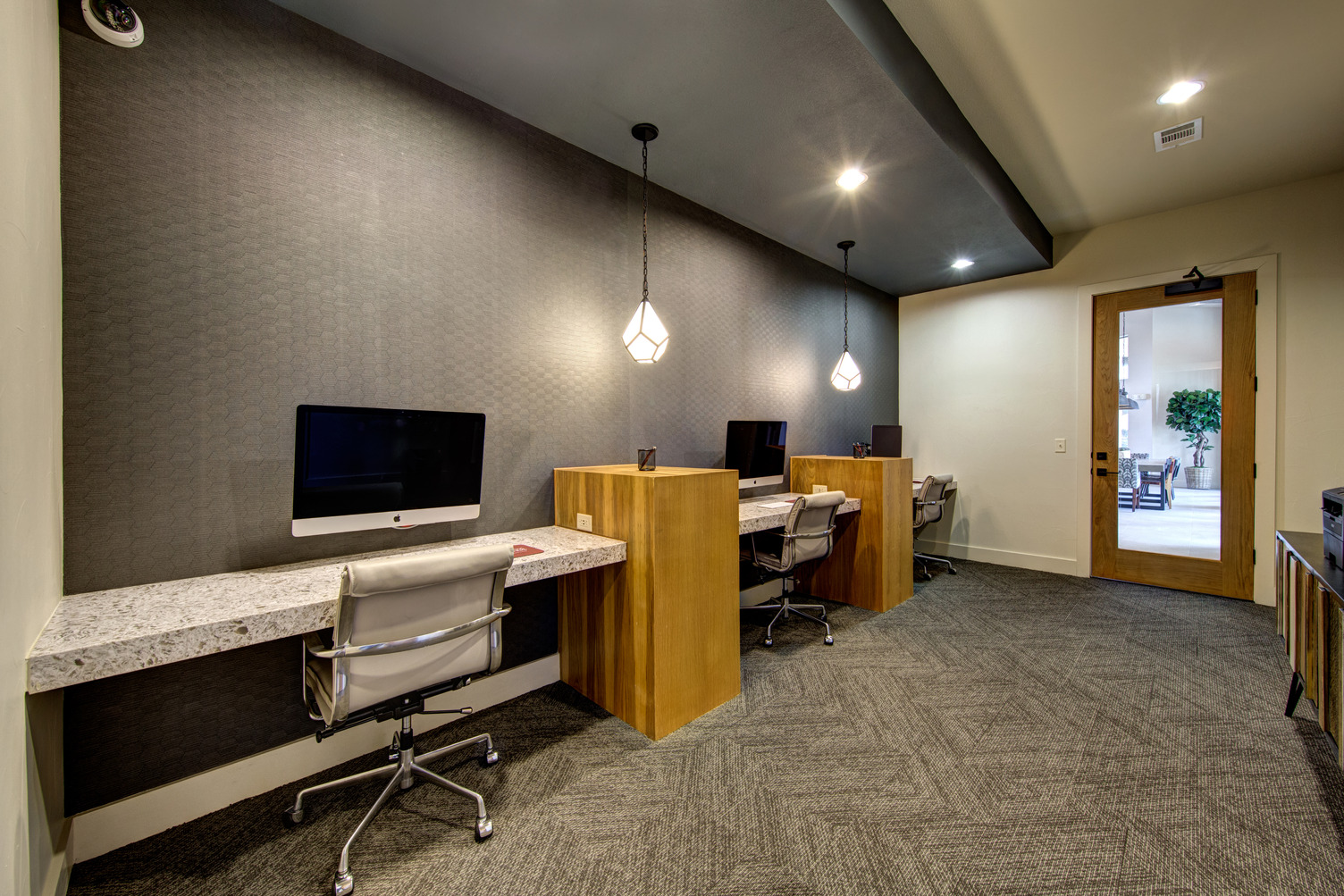 Business center with swivel chairs, three workstations with iMac, and door leading to courtyard