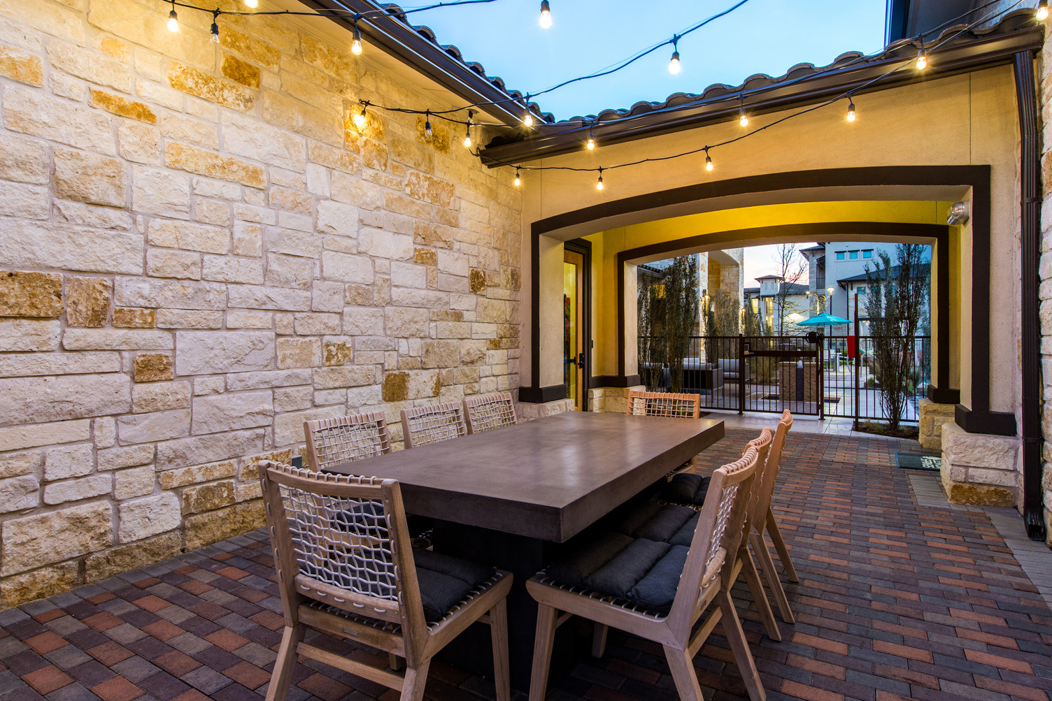 Private outdoor dining area at dusk with large table, chairs, and festival lights