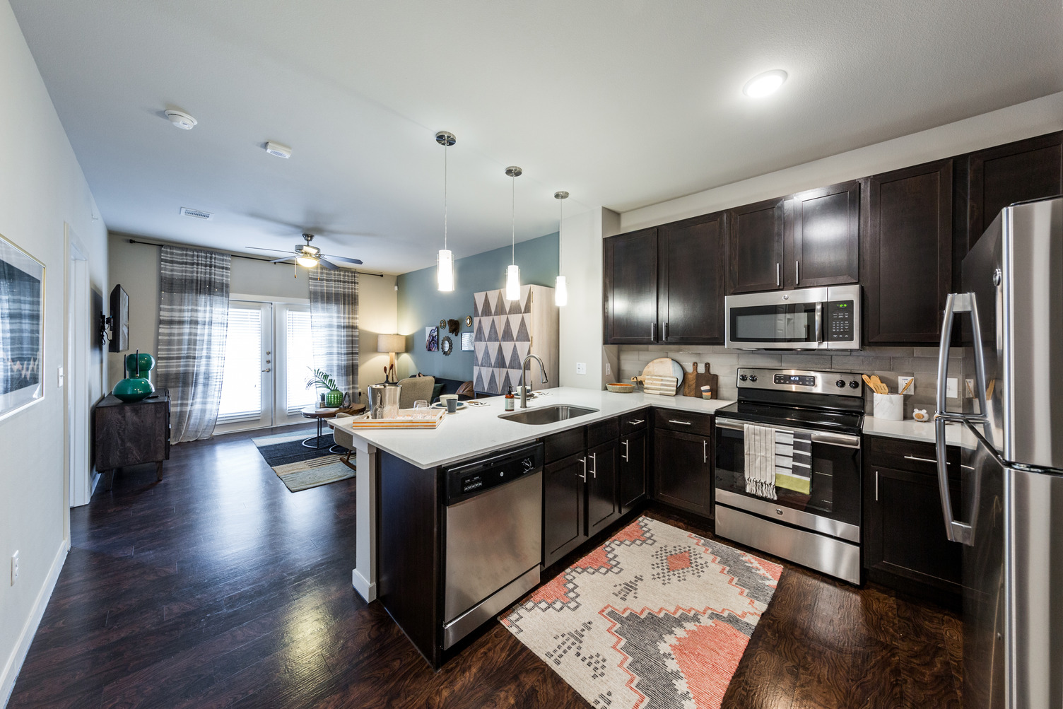 Model apartment with dark wood flooring, dark cabinets, and stainless steel appliances with pendant lighting over quartz counters