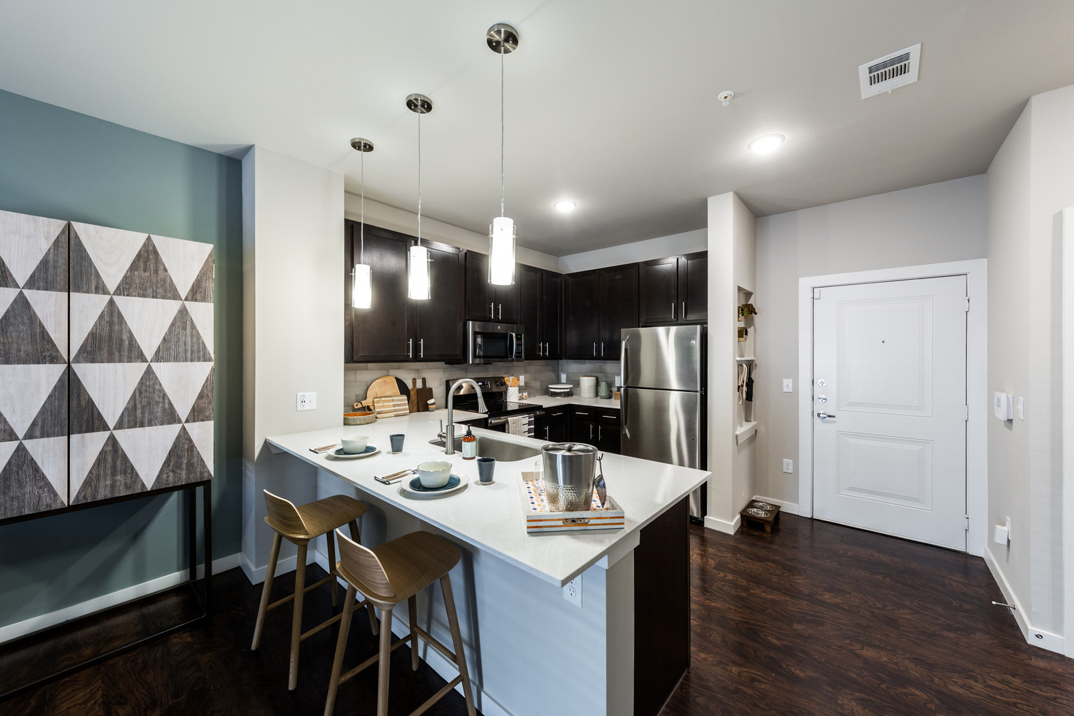 Model apartment kitchen with barstool seating, undermount sink, and dark kitchen cabinets
