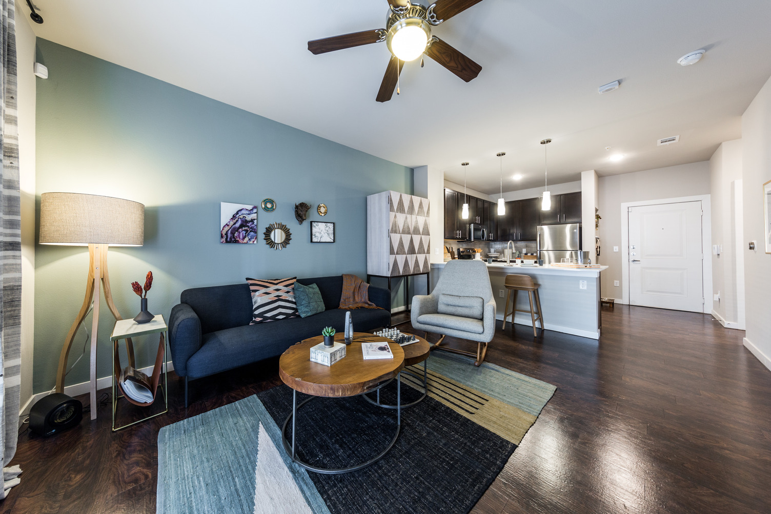 Model apartment living room with wood-style flooring, ceiling fan, loveseat, and armchairs