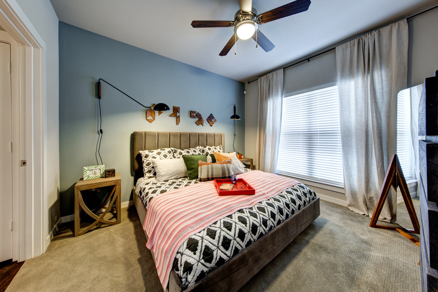 Model apartment bedroom with queen bed, ceiling fan, and carpeting