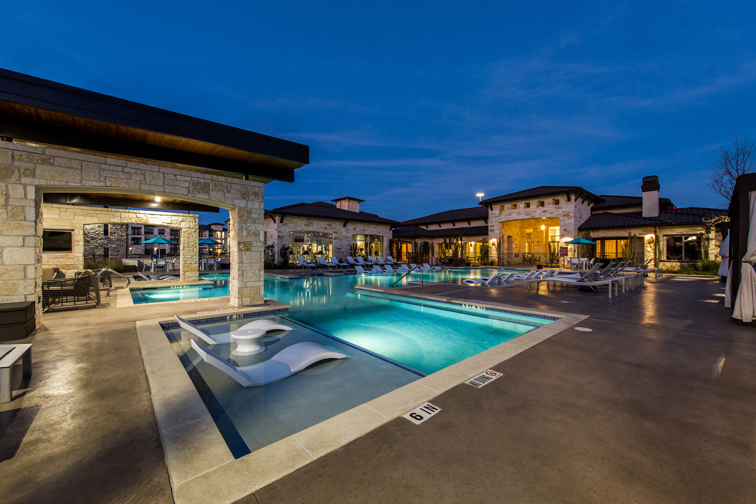Evening view of resort-style swimming pool courtyard with lounge seating and landscaping