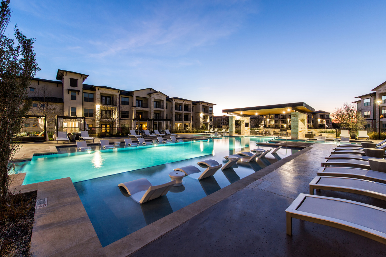 View of in-pool loungers at dusk in large pool courtyard