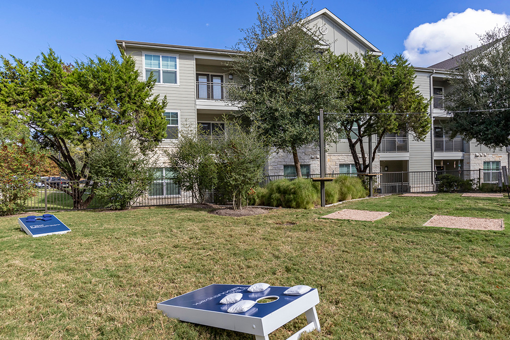 Outdoor park area with cornhole game near planted trees and garden