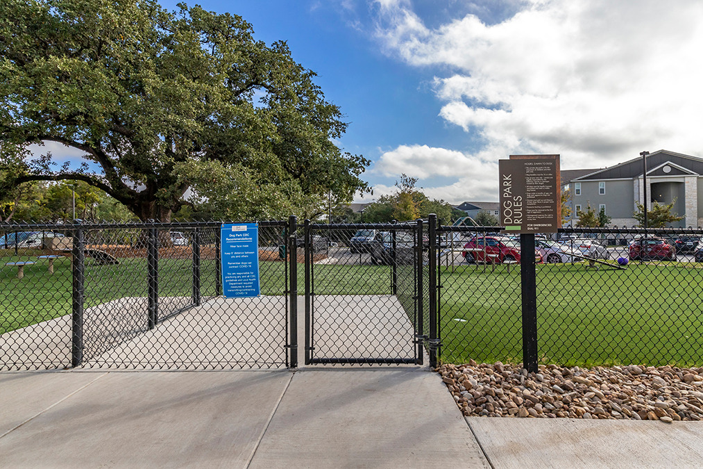 Outside gated dog park area with obstacles and signs for rules