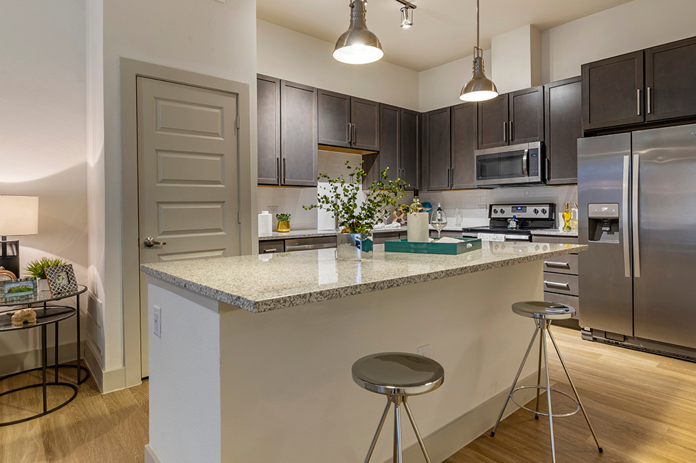 Model apartment kitchen with island, designer pendant lighting, stainless steel appliances, and pantry